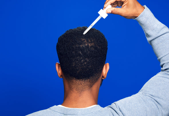 Back of a man’s head while applying men’s Rogaine Topical Solution on a blue background.