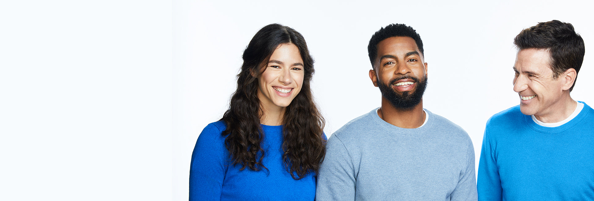 Woman with long brown hair and two men smiling in blue sweaters on a white background.