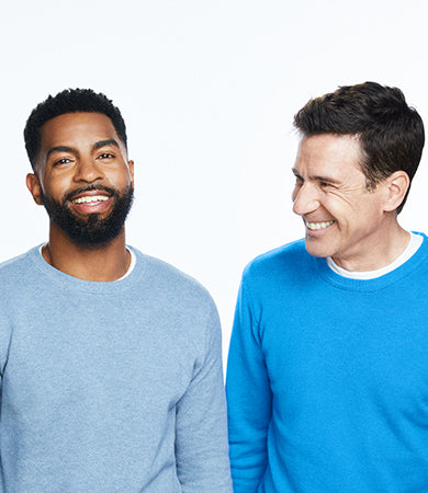 Woman with long brown hair and two men smiling in blue sweaters on a white background.