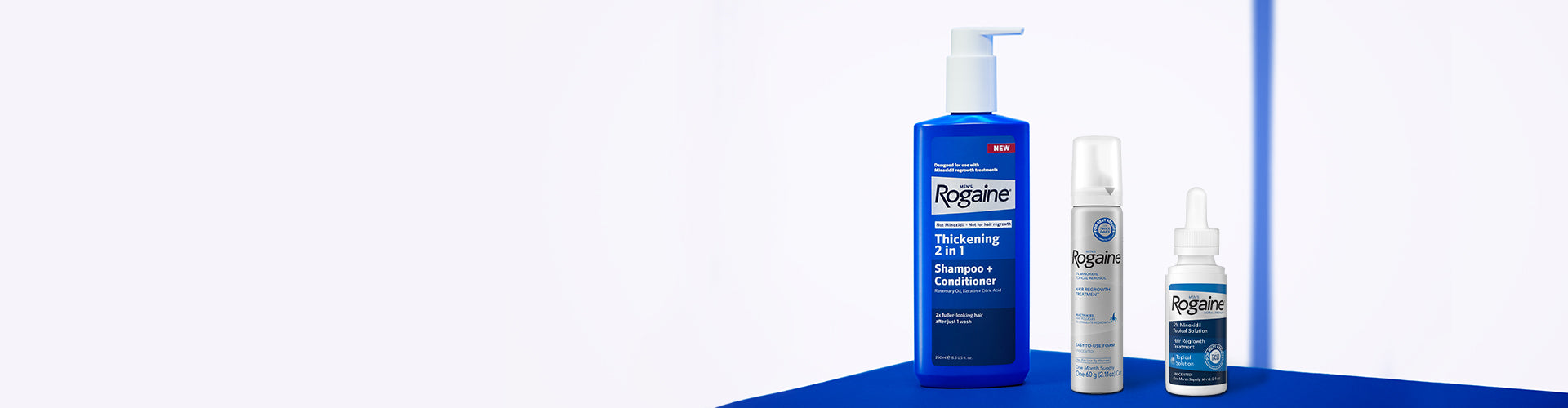 Men's Rogaine Thickening 2 in 1 Shampoo + Conditioner and Foam and Topical Hair Regrowth Treatments on a blue counter with a white background.