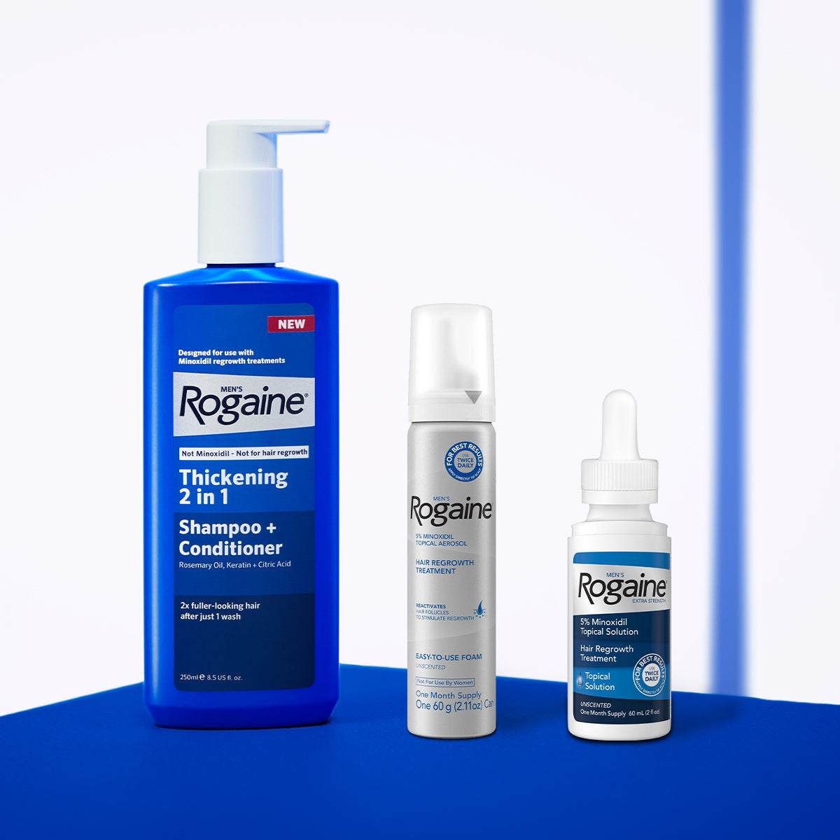 Men's Rogaine Thickening 2 in 1 Shampoo + Conditioner and Foam and Topical Hair Regrowth Treatments on a blue counter with a white background.