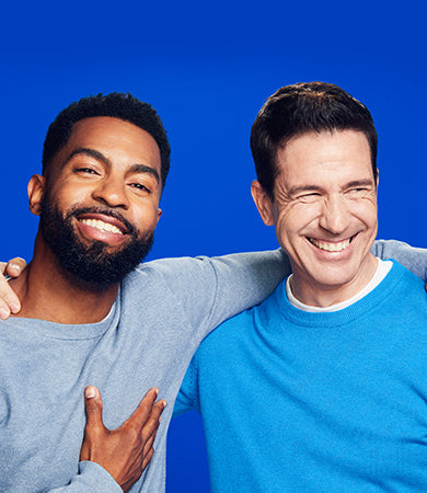 Two men in blue sweaters smiling on a blue background.