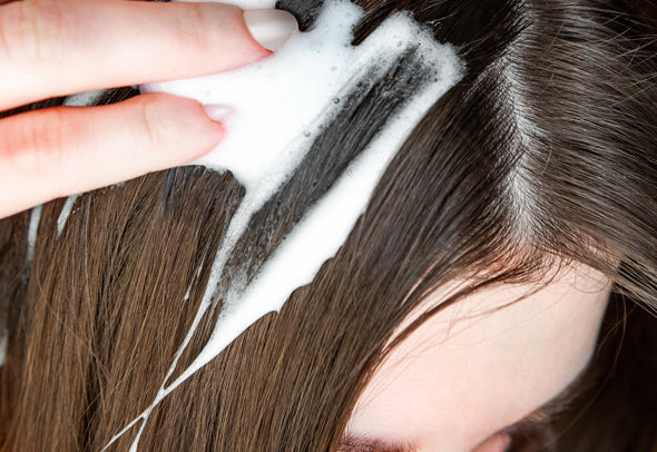 Close up of the top of a woman’s head with long brown hair applying woman’s Rogaine Foam.