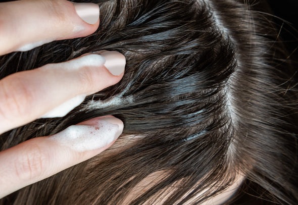 A woman with long brown hair massaging her scalp with her fingers